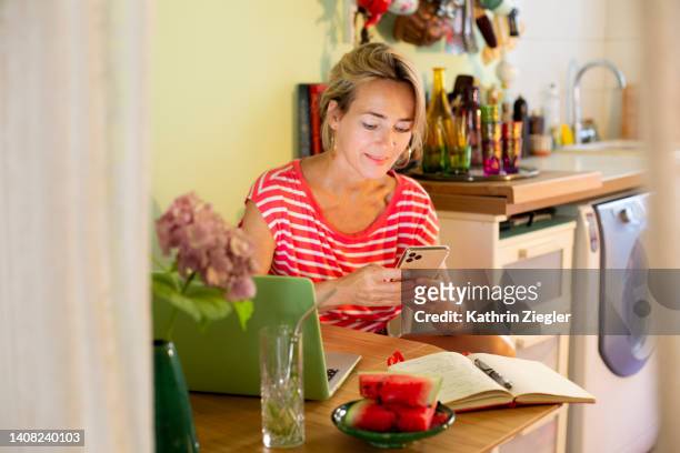 woman working at kitchen table, text messaging on mobile phone - hydrangea lifestyle stockfoto's en -beelden