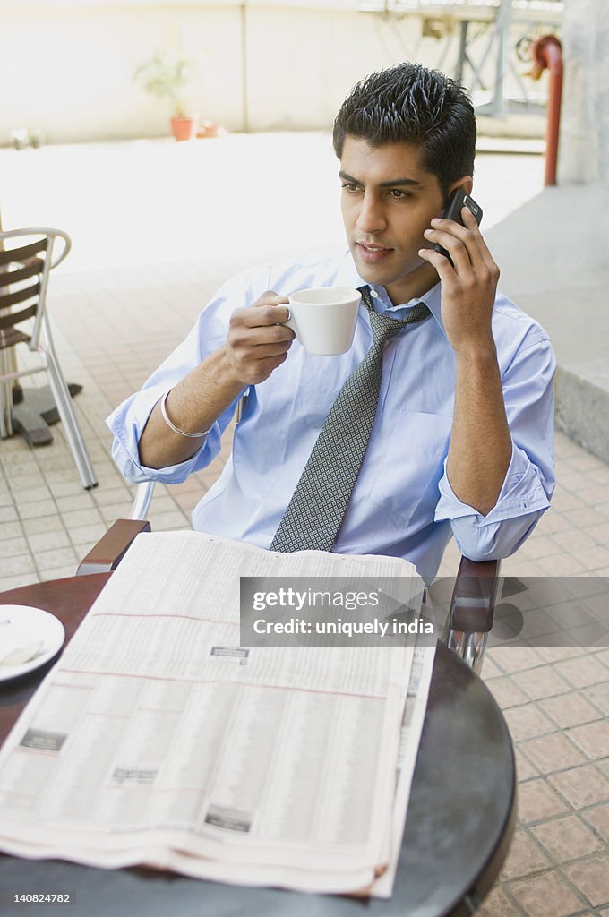 Businessman drinking coffee while talking on a mobile phone, Gurgaon, Haryana, India