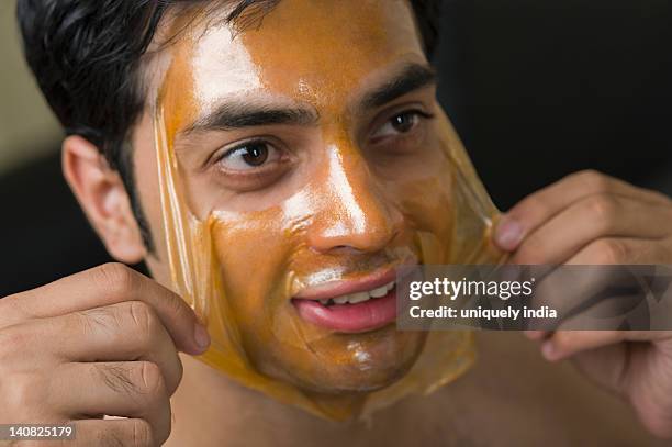 close-up of a man peeling off facial mask from face - peel off mask stock-fotos und bilder