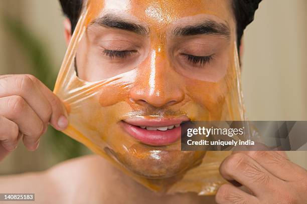 close-up of a man peeling off facial mask from face - peel off mask stock-fotos und bilder