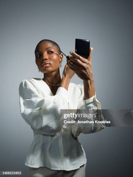 young female model applying mascara in compact mirror - eye make up stock pictures, royalty-free photos & images