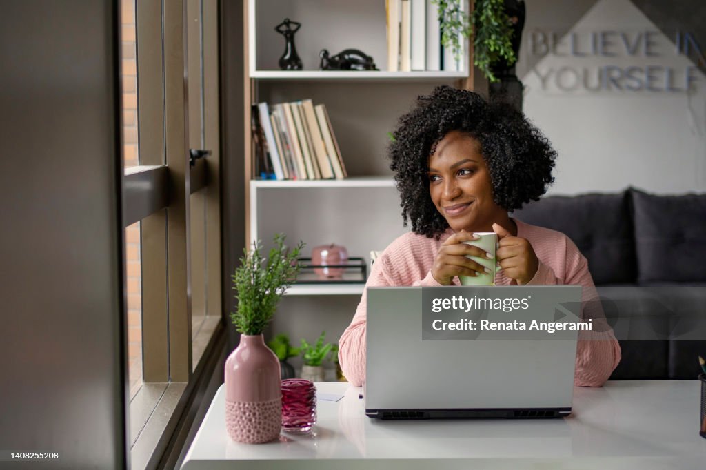 African American woman drinking tea while working on laptop