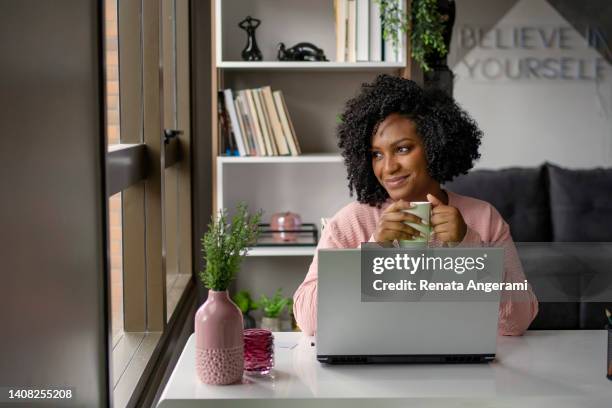 african american woman  drinking tea while working on laptop - pleased laptop stock pictures, royalty-free photos & images