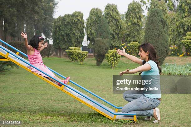 woman catching her daughter at bottom of a slide - sliding foto e immagini stock