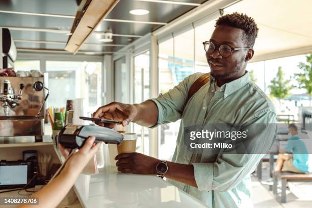 un joven afroamericano pagando en la cafetería - pago por móvil fotografías e imágenes de stock