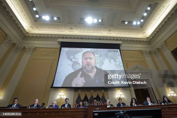 Far right radio show host Alex Jones appears on a video screen during videotaped testimony above members of the Select Committee to Investigate the...