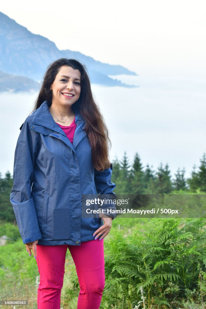 Portrait of smiling young woman standing on field against sky