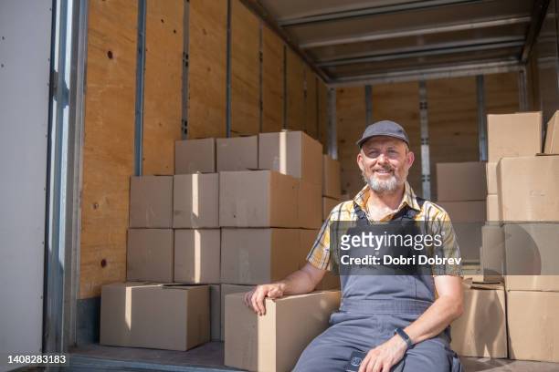 a cheerful worker sits and rests in the cargo hold of a truck full of cartons. - tradesman van stock pictures, royalty-free photos & images