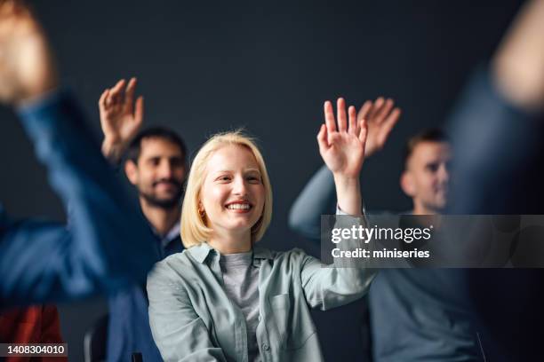 portrait of a pretty woman raising her hand on a seminar and smiling - questioning stock pictures, royalty-free photos & images