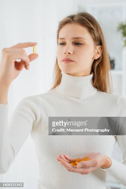 beautiful young female looks at the pill omega-3 holding in his hand - hand holding several pills photos et images de collection