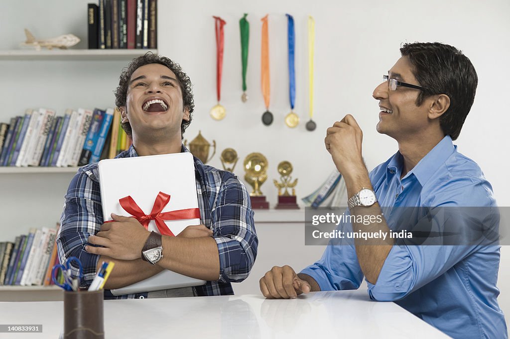 Man laughing and hugging a laptop gifted by his father