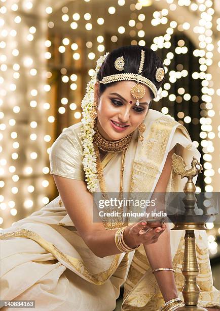 indian woman in traditional clothing lighting an oil lamp - onam foto e immagini stock