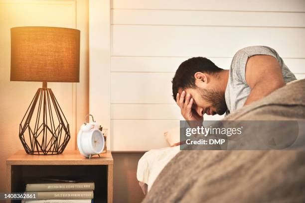 young displeased, tired man with insomnia unable to sleep and suffering from burnout and fatigue struggling to get up out of bed in the morning. mentally exhausted male awake in bed feeling stressed - dust bildbanksfoton och bilder