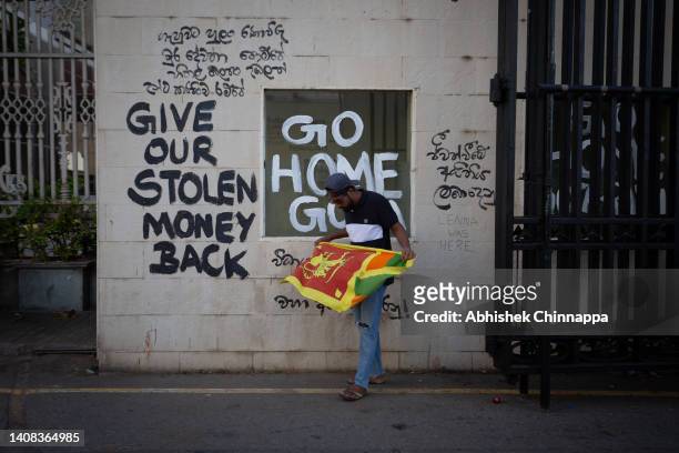Protester unfurls the Sri Lankan national flag at the vandalized gateway of the presidential palace on July 13, 2022 in Colombo, Sri Lanka. Sri...
