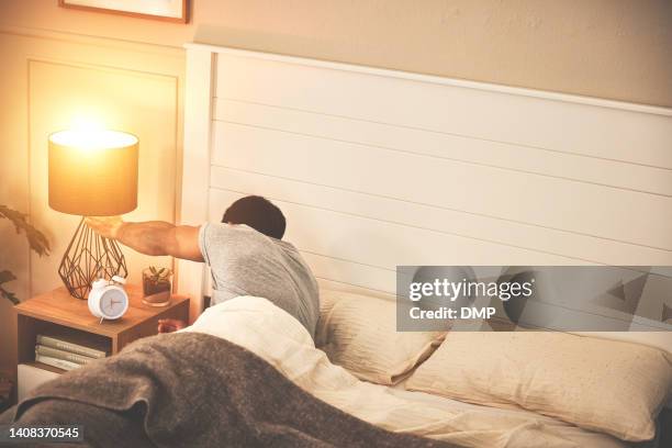 tired man suffering with insomnia and waking up early after rest in his bedroom. sleepless male switching off bedside lamp before taking a nap. falling asleep to rest before work in the morning - bedside table lamp stock pictures, royalty-free photos & images