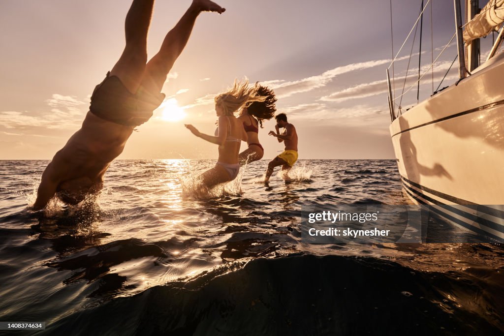 Carefree people jumping into sea from boat at sunset.