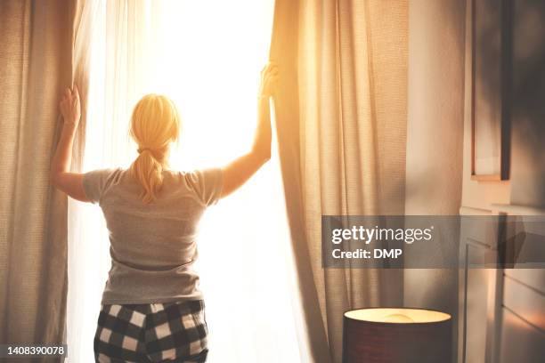 vue arrière d’une femme ouvrant les rideaux un matin d’été lumineux au lever du soleil à l’intérieur de sa chambre. la femelle ouvre les rideaux pour laisser entrer la lumière du soleil dans sa chambre. dame en pyjama éveillée et prête pour  - mur maison ombres photos et images de collection