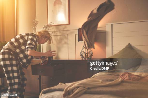 anxious woman rushing to get dressed after oversleeping.
a stressed young female in pajamas searching for an outfit in her drawers as she is late for work. frustrated woman throwing clothes in a rush - kings of chaos in south africa stockfoto's en -beelden