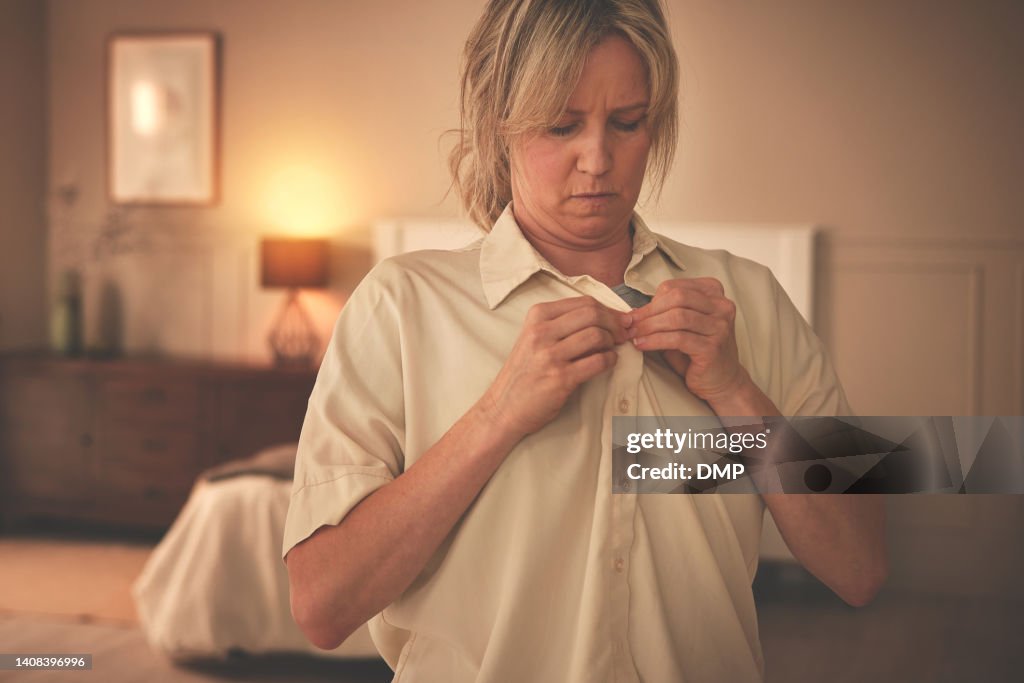 Mature woman dressing and putting on fresh clothing while preparing for an interview. One female getting dressed and buttoning her shirt in the bedroom. Freshening up and getting ready for work