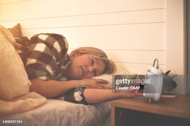 tired woman looking at alarm clock, waking up late in the morning before work. depressed, exhausted older female worrying about problems in bed. insomnia from being overworked and fatigued - struggle stock pictures, royalty-free photos & images