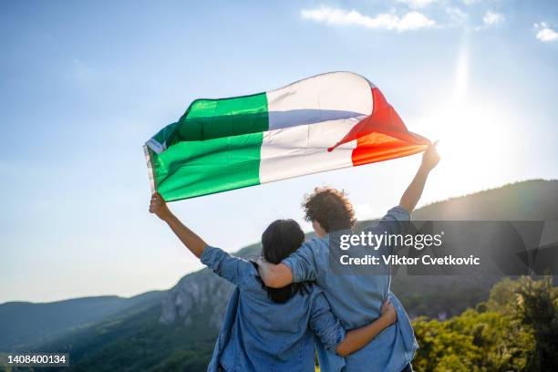 happy couple holding italian national flag on top of the hill, rear view - italiaanse vlag stockfoto's en -beelden