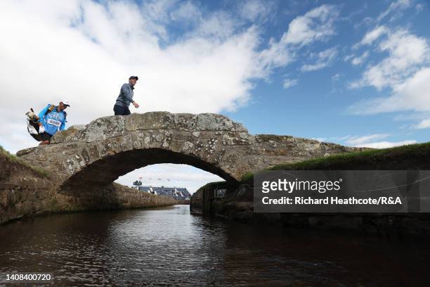 Rory McIlroy of Northern Ireland and their Caddie walk across the Swilcan Bridge on the 18th hole during a practice round prior to The 150th Open at...