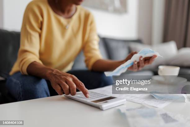 primer plano de una mujer mediana adulta revisando sus facturas de energía en casa, sentada en su sala de estar. ella tiene una expresión preocupada - recibo fotografías e imágenes de stock