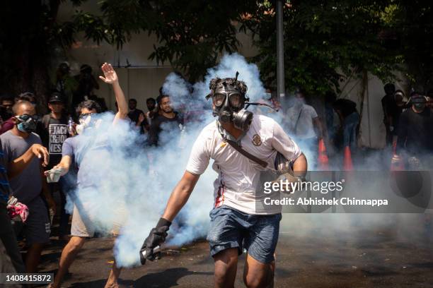 Protestor wearing a gas mask runs to throw a tear gas canister fired by army personnel during a protest seeking the ouster of Sri Lanka's Prime...