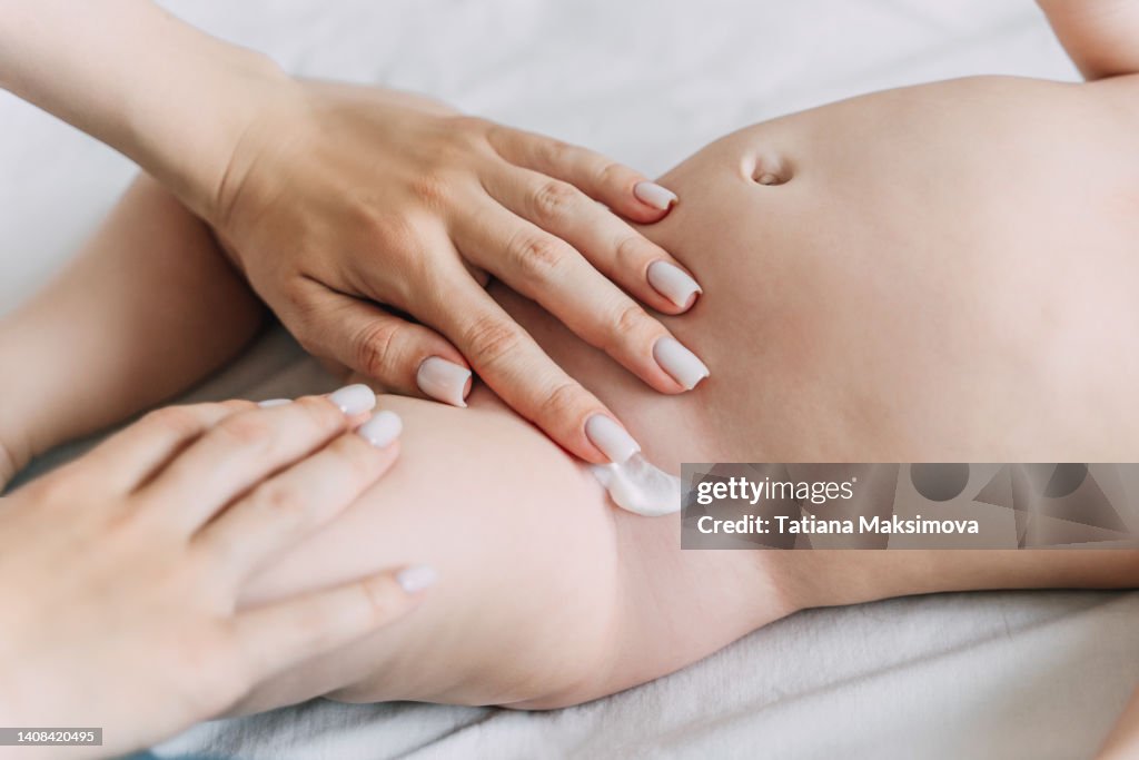 Mother smears the baby's folds with diaper rash cream under the diaper.
