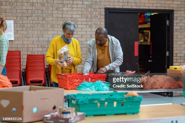 senior volunteers at a food bank - homelessness help stock pictures, royalty-free photos & images