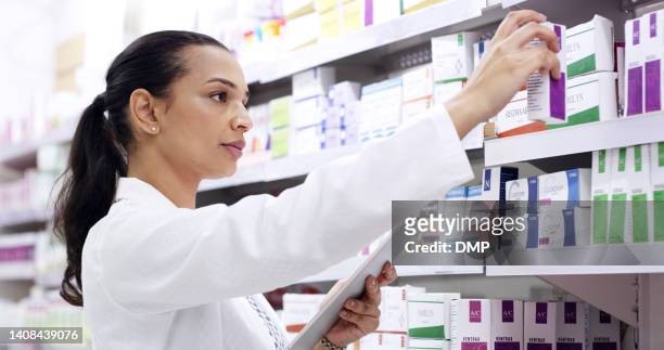 pharmacist using digital tablet in a pharmacy while counting and sorting an inventory of retail medicine on shelves. young woman using technology to stay organised while doing stocktake in a chemist - pharmacist stock pictures, royalty-free photos & images