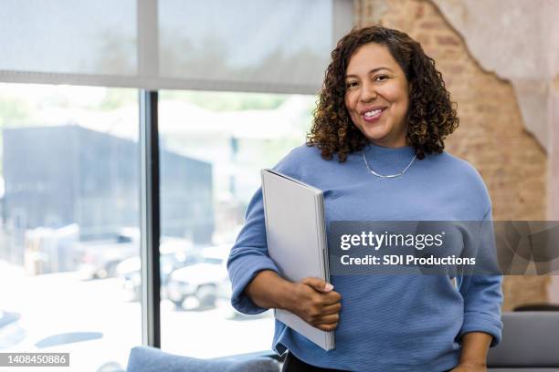 female businesswoman holds laptop and smiles for camera - personnel carrier stock pictures, royalty-free photos & images
