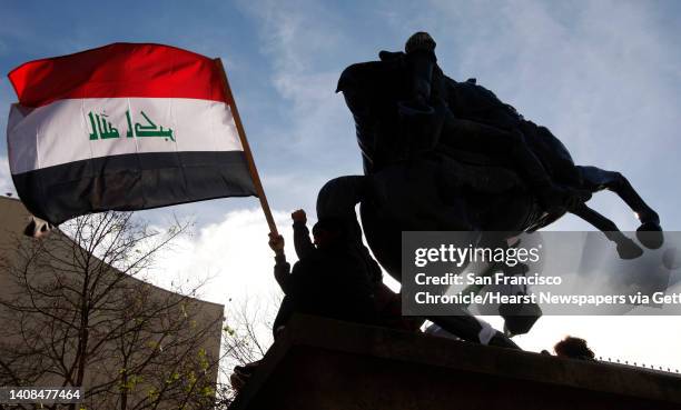 Demonstrators wave an Iraqi flag from the base of a statue during a rally Saturday at San Francisco's UN Plaza attended by thousands of people in...