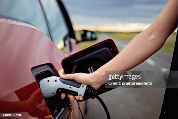 woman is plugging/unplugging cable to electric car - fuel efficiency stock pictures, royalty-free photos & images