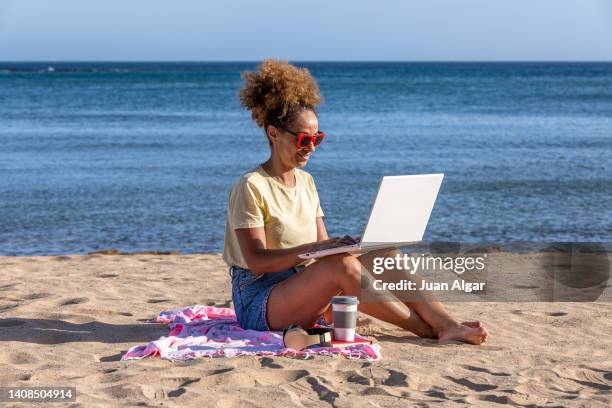 hispanic woman browsing laptop on beach - laptop netbook fotografías e imágenes de stock