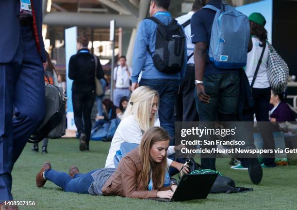 Kristin Richter and Katie Owen sprawl out on artificial grass to do some work in front of Moscone Center South at the Dreamforce conference hosted by...