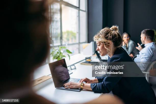 businesspeople sitting in a row at office desk and working on their laptop computers - co working space stock pictures, royalty-free photos & images