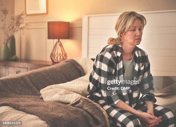 sad and depressed woman suffering from insomnia deep in thought sitting on a bed while her husband sleeps in the background. worried wife contemplating divorce or separation due to infidelity problem - sighing stock pictures, royalty-free photos & images