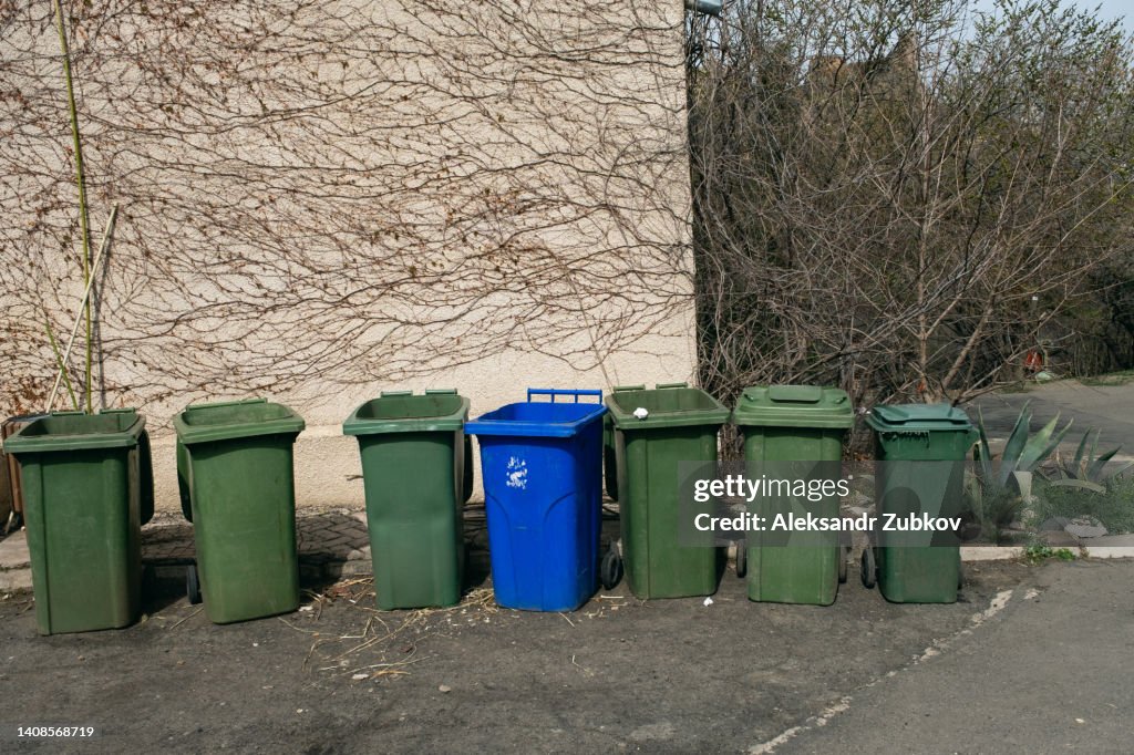 Plastic garbage cans or dumpsters, tanks on wheels for moving and transporting, stand in a row on the street. The concept of environmental protection, sustainable lifestyle. Recycling of garbage.