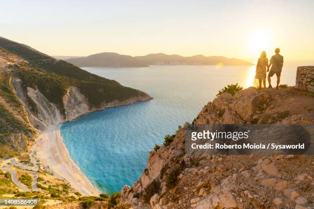 couple holding hands watching sunset on cliffs, greece - cefalónia imagens e fotografias de stock
