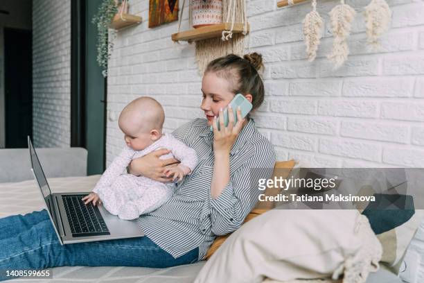 working mother concept. woman and baby girl work on laptop at home and using phone. - call to arms stock pictures, royalty-free photos & images