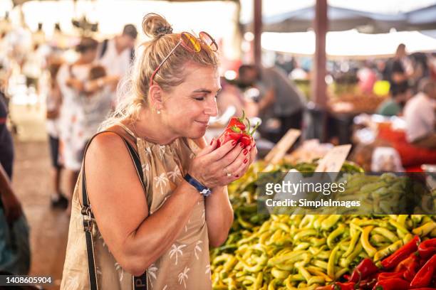 an adult woman buys vegetables at the market, tests the freshness of peppers by smell. - spice market stock pictures, royalty-free photos & images