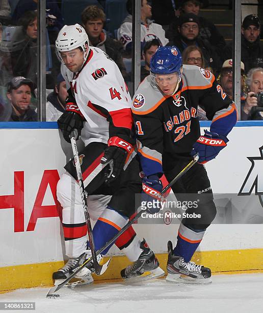 Chris Phillips of the Ottawa Senators and Kyle Okposo of the New York Islanders battle for the puck at Nassau Veterans Memorial Coliseum on February...