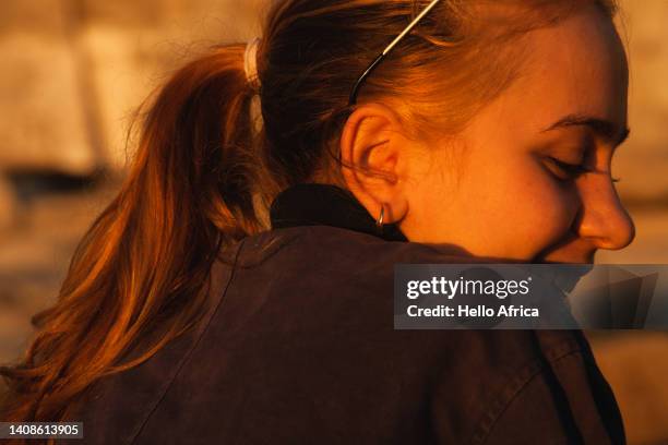 profile view of a beautiful smiling young woman, a teenager with long blond hair tied back in a ponytail looks back over her shoulder with the lovely golden light of sunshine at dusk or dawn illuminating her face - hispanic man profile hopeful stock-fotos und bilder