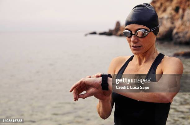 beautiful female swimmer checking her fitness tracker watch after a swim in ibiza - checking sports fotografías e imágenes de stock