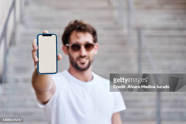 young man in basic white t-shirt showing a mobile phone with white screen. image for mockup. - white shirt template stock pictures, royalty-free photos & images