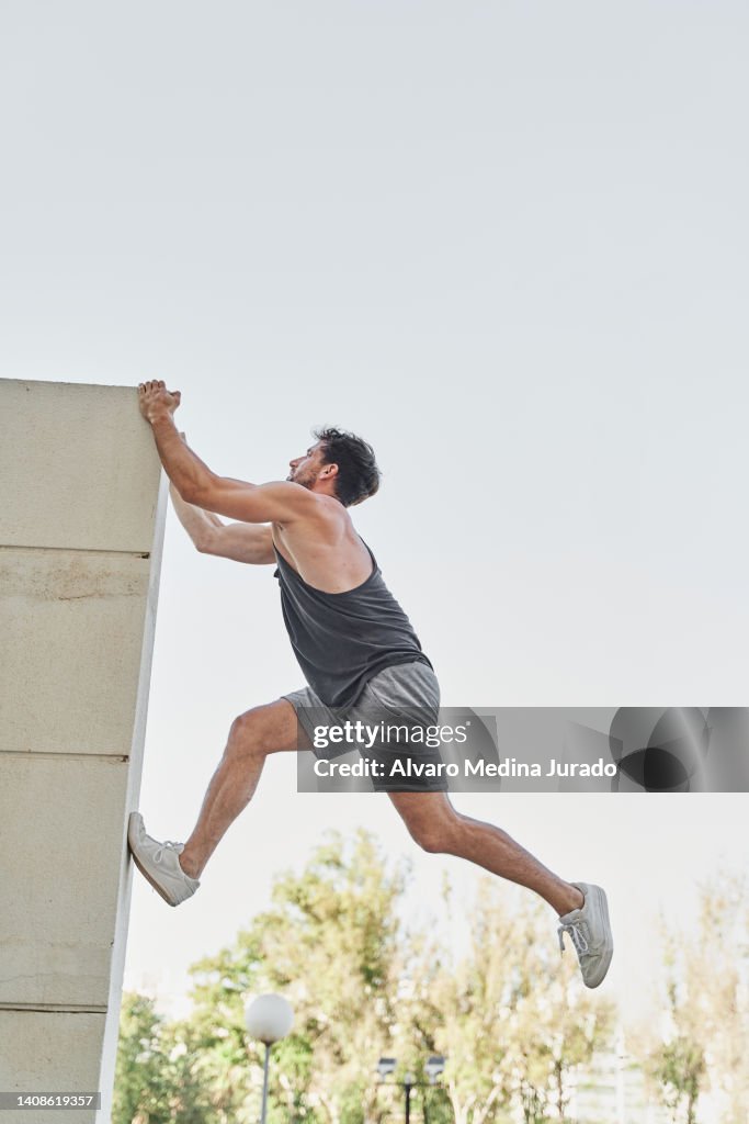 Young man practicing parkour dressed in sportswear climbing a ledge of a building in the city. Urban sports concept.