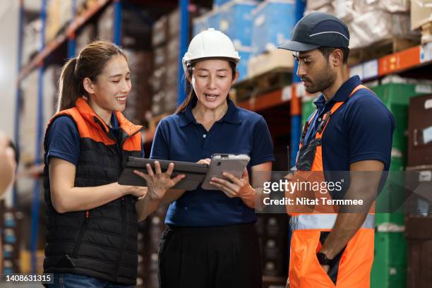 manage and improve warehouse operations. asian female warehouse manager having discussing with her team in aisle of shelf rack in a distribution warehouse while explaining about standard operation improvement to increased warehouse efficiency. - storage solutions stock pictures, royalty-free photos & images