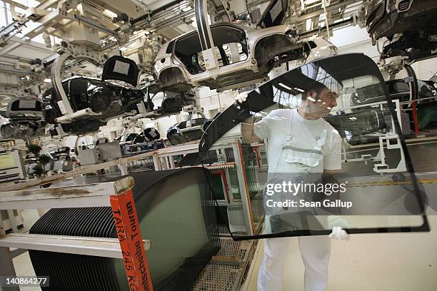 Worker carries a windshield during the assembly of Volkswagen Touran and Tiguan cars at the Volkswagen factory on March 7, 2012 in Wolfsburg,...
