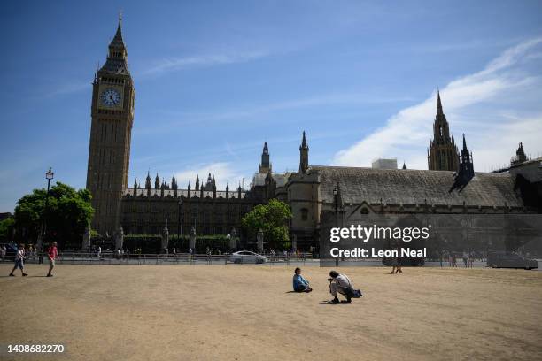 Tourists walk on the sun-baked Parliament Square on July 14, 2022 in London, England. Usually grass-covered, the heat has seen the grass dry and die....